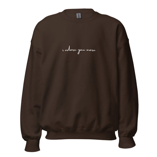 Dark chocolate crewneck sweatshirt with white text reading “i adore you more,” centered on the chest